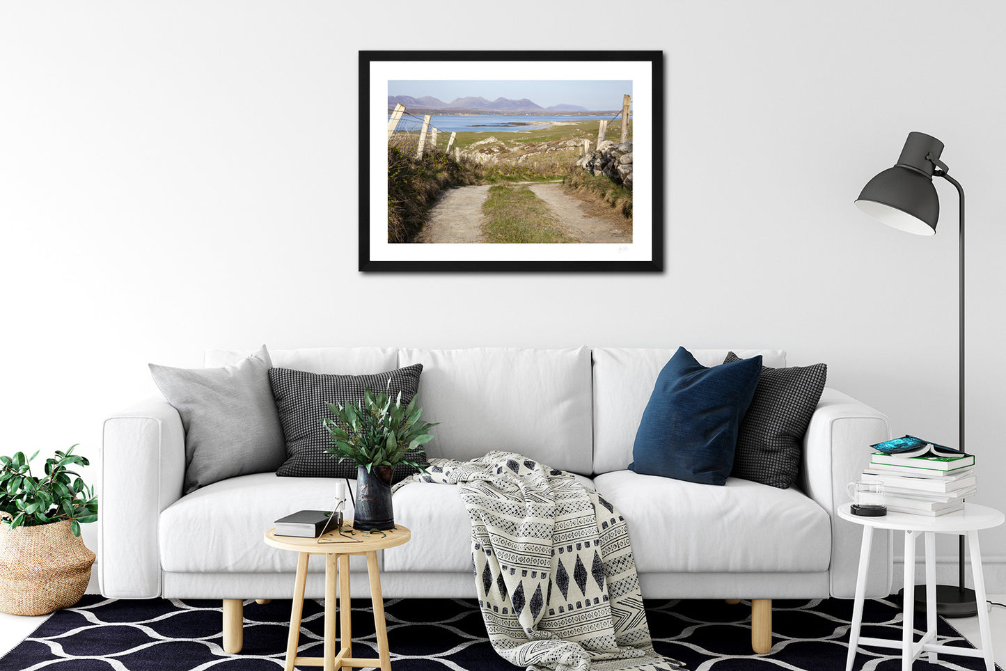 a framed fine art photograph of the view from a narrow country road in Mannin Beg, Connemara looking across Mannin Bay at the 12 Bens mountain range hanging on a while wall abov a large white sofa