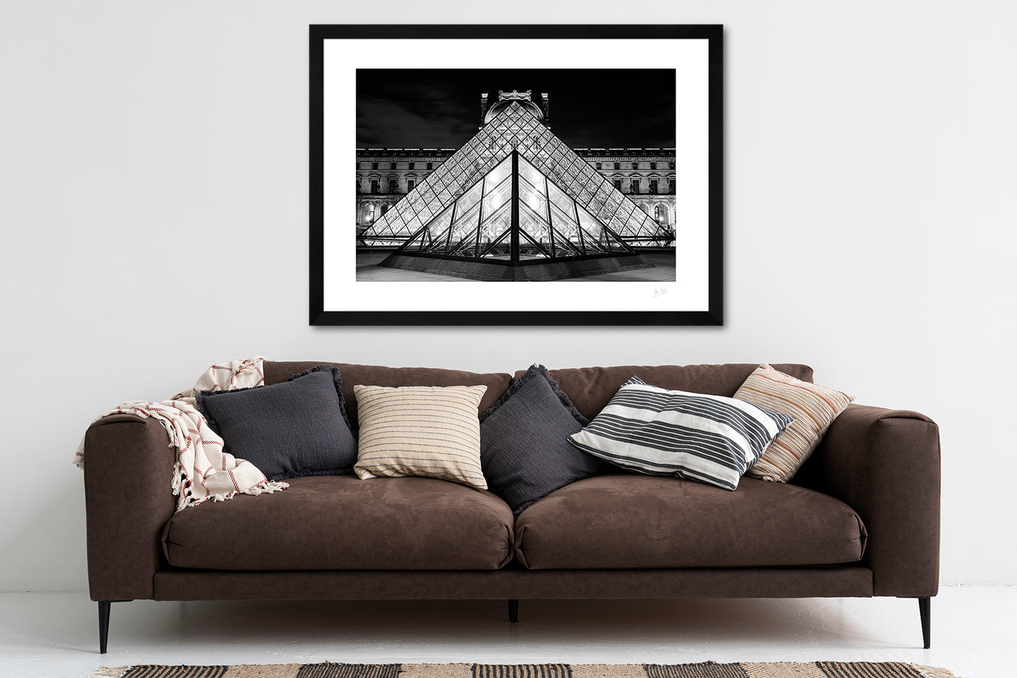 a framed black and white fine art photoraphic print of the old and the new facades of the Louvre museum lined up in perfect symmetry, hanging on a living room wall above a sofa