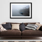 a framed fine art photograph of a rowing boat moored in Roundstone Harbour, Connemara in dense fog with only a few of the towns buildings visible hanging on a white wall above a big brown sofa 