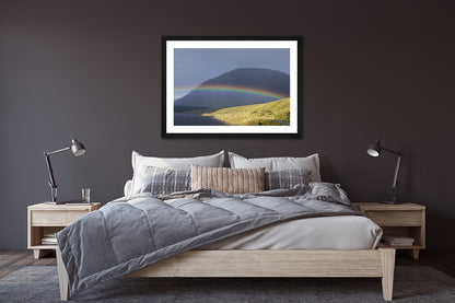 a framed fine art photographic print of a rainbow stradling Lough Inagh, Connemara as the rain shower moves away toward Letterbreckaun Mountain, hanging on a wall over a bed