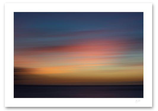 An abstract photographic art print featuring a twilight scene with deep blue, pink, orange, and yellow sky over a dark horizon, presented with a wide white border.