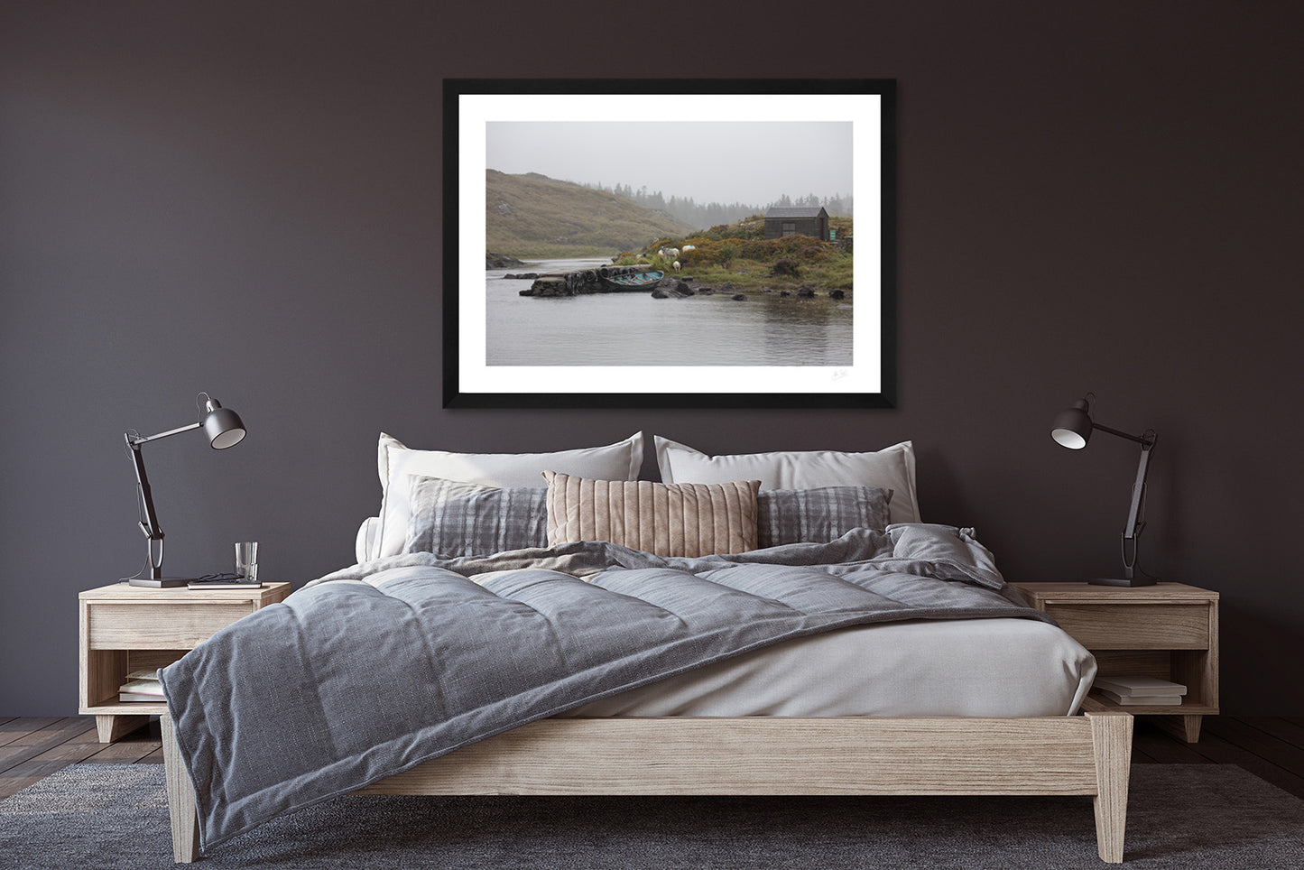 a framed fine art photograph of a fishing hut and row boat mooring on the Owenmore River on a rainy day with a few grazing sheep hanging on a dark bedroom wall above a wooden double bed