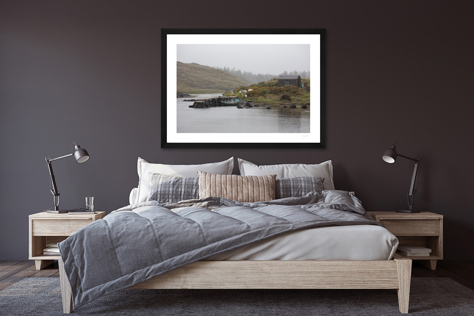 a framed fine art photograph of a fishing hut and row boat mooring on the Owenmore River on a rainy day with a few grazing sheep hanging on a dark bedroom wall above a wooden double bed