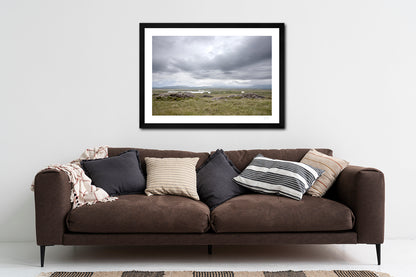 a framed fine art photographic print of a lone sheep surveying the bog lands on a damp and grey day along The Bog Road in Connemara, hanging on a wall above a brown sofa