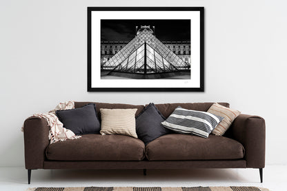  a framed black and white fine art photoraphic print of the old and the new facades of the Louvre museum lined up in perfect symmetry, hanging on a living room wall above a sofa