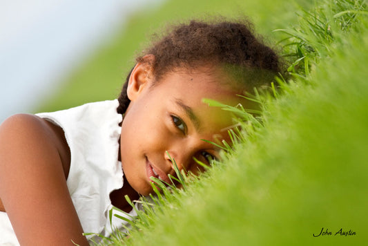 headshot portrait of a young girl lying on the green grass of summer 