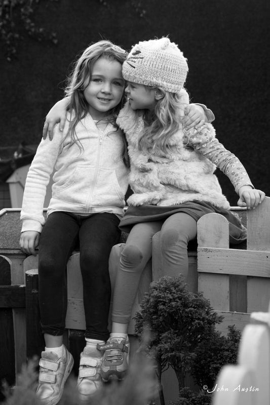 A black and white photo of two young girls sharing a happy moment sitting on a wall