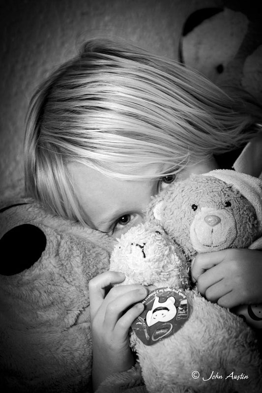 A headshot of a young boy hiding behind his favourite teddy